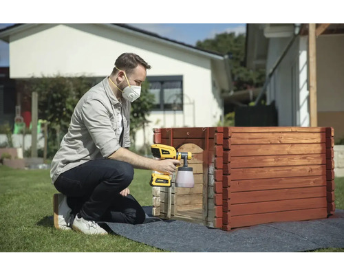 Muž stříká dřevo stříkací pistolí na barvy na zahradě.