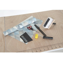 Tapeta s geometrickým vzorem, štětka na lepidlo, přítlačný váleček, tapetovací nůž, přítlačná špachtle a nůžky na stole.