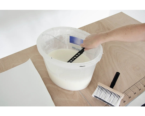 Lepidlo na tapety se míchá v kbelíku s míchadlem, vedle leží štětka na tapety a tapeta.