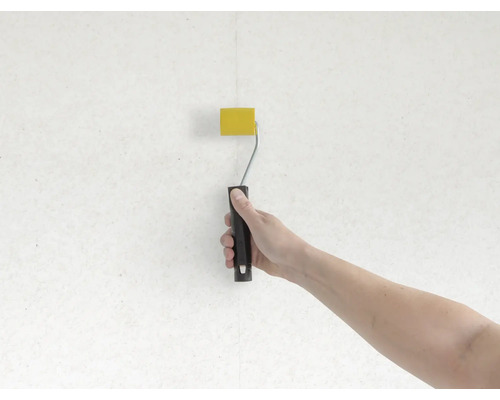 Ruka maluje stěnu válečkem na barvu žlutě