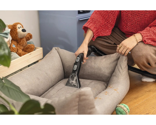 Osoba čistí pelíšek pro psy pomocí vysavače na mokré čištění.
