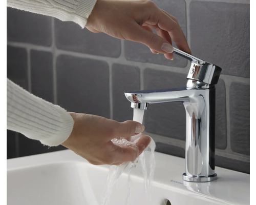 Osoba používá chromovanou umyvadlovou baterii nad umyvadlem.