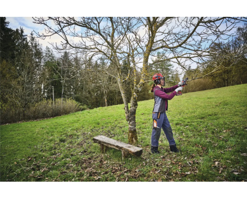 Žena s ochrannou přilbou stříhá strom nůžkami na větve v zahradě.