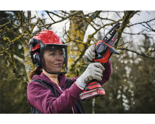 Žena s ochrannou helmou a akumulátorovou řetězovou pilou prořezává strom