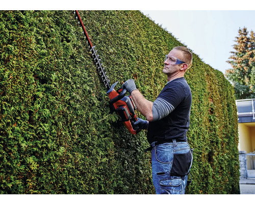 Muž stříhá živý plot pomocí nůžek na živý plot a má přitom ochranné brýle.