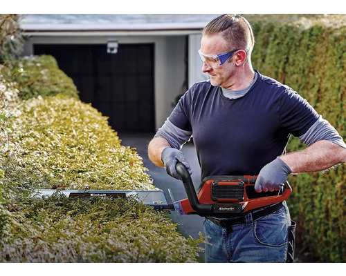 Muž stříhá živý plot elektrickými nůžkami na živý plot od společnosti Einhell.
