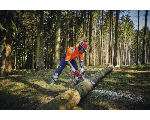 Osoba v ochranném oděvu řeže motorovou pilou kmen stromu v lese.