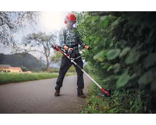 Osoba stříhá živý plot pomocí akumulátorového vyžínače a ochranného oděvu