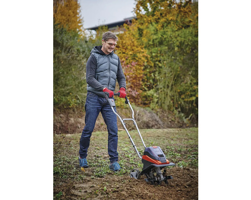 Muž používá motorový kultivátor na zahradě k obdělávání půdy.