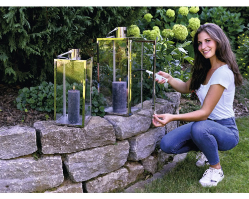 Žena zapaluje svíčku ve svícnu na zahradě