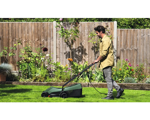 Muž seče trávník elektrickou sekačkou na zahradě.