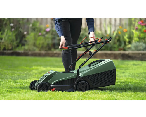 Osoba obsluhuje zelenou sekačku na trávníku.