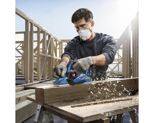 Řemeslník používá elektrický hoblík Bosch k hoblování kusu dřeva.