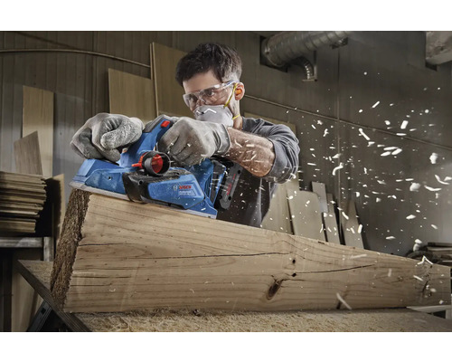 Muž hobluje dřevěnou desku elektrickým hoblíkem značky Bosch