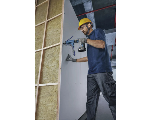 Řemeslník připevňuje sádrokartonovou desku pomocí šroubováku se zásobníkem ke zdi