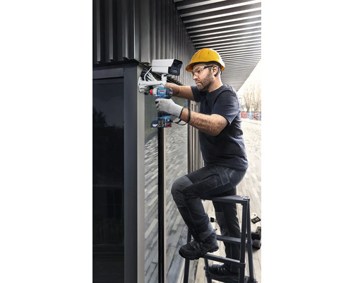 Řemeslník montuje bezpečnostní kameru pomocí akumulátorového šroubováku na žebřík.