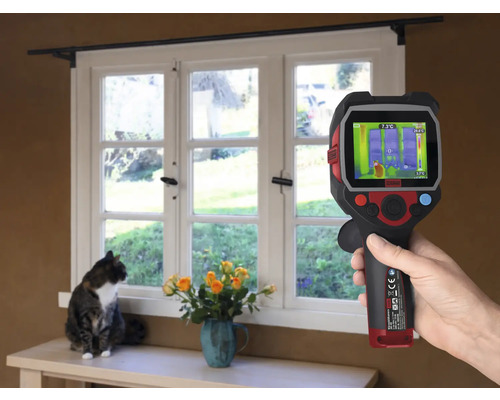 Ruka drží termokameru před oknem, zatímco kočka sedí na parapetu.