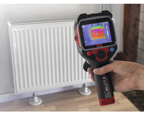 Ruka drží termokameru před radiátorem pro měření teploty.