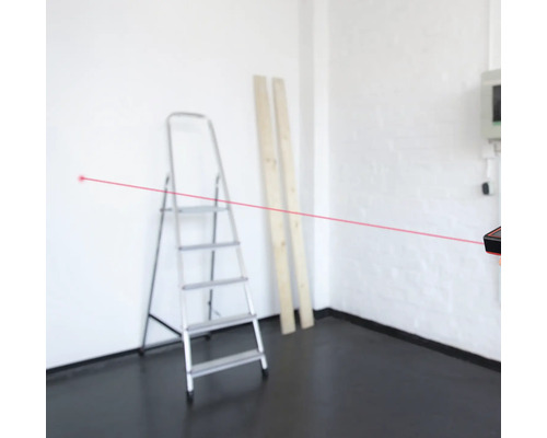 Pohled do místnosti s laserovým dálkoměrem pro měření vzdáleností, v pozadí žebřík a dvě dřevěné desky