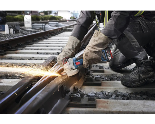 Pracovník řeže úhlovou bruskou železniční trať, přičemž vznikají jiskry.
