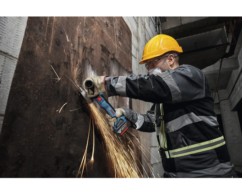 Dělník s akumulátorovou úhlovou bruskou řeže kov