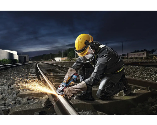Pracovník brousí železniční kolejnici úhlovou bruskou a jiskří.