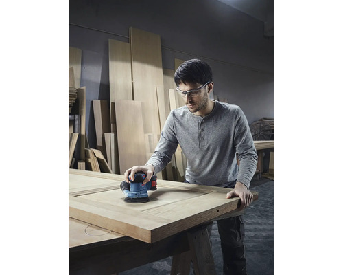 Muž brousí dřevěné dveře excentrickou bruskou v dílně