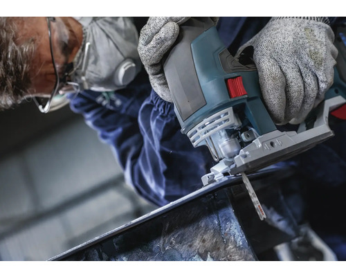 Muž řeže kov přímočarou pilou. Má na sobě ochranné brýle, obličejovou masku a rukavice.