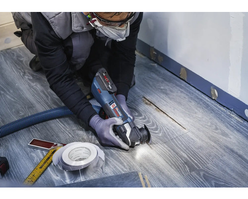 Řemeslník používá multifunkční nástroj na laminátové podlaze pro renovaci.