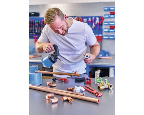 Muž pájí měděné trubky s pájecí lampou a pájkou v dílně.