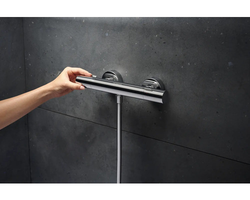 Nástěnný sprchový termostat s ručním ovládáním před tmavou stěnou