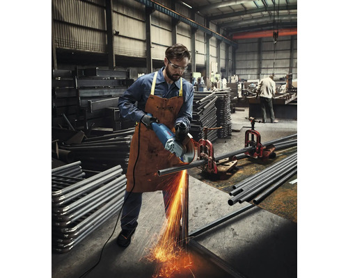 Muž v dílně řeže úhlovou bruskou kovovou trubku, od které odlétávají jiskry.