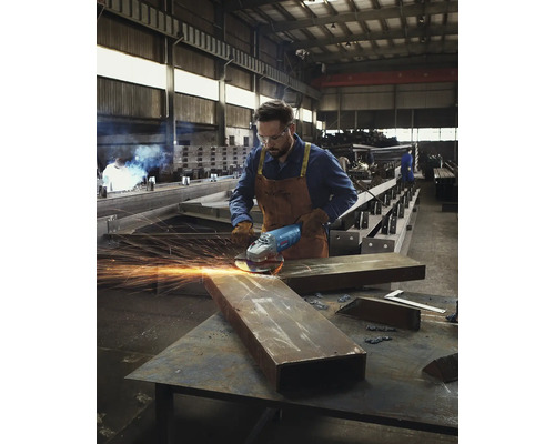 Muž brousí kov úhlovou bruskou v dílně.