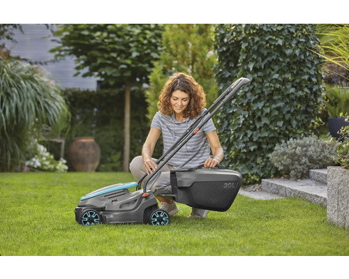 Žena klečí v zahradě a montuje sekačku na trávu s 30litrovým sběrným košem.