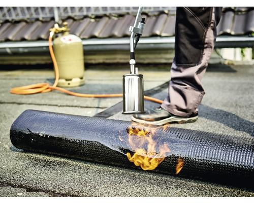 Pokrývač svařuje bitumenový pás s hořákem a plynovou lahví.