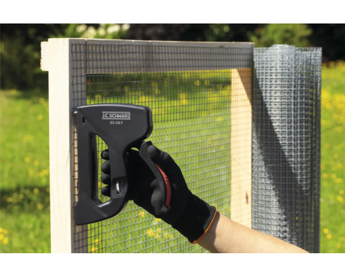 Osoba připevňuje drátěné pletivo ke dřevěnému rámu pomocí sponkovačky J.C. Schwarz JCS-530 P