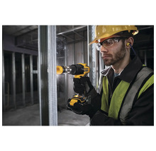 Muž vrtá vrtačkou otvor do kovové stěny. Má ochranné brýle, helmu a špunty do uší.