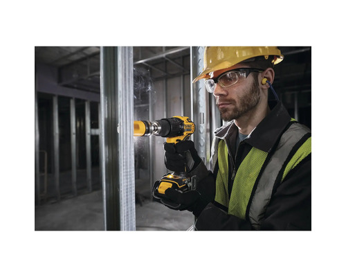 Muž vrtá vrtačkou otvor do kovové stěny. Má ochranné brýle, helmu a špunty do uší.