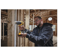 Řemeslník vrtá vrtačkou Dewalt do dřeva v hrubé stavbě.