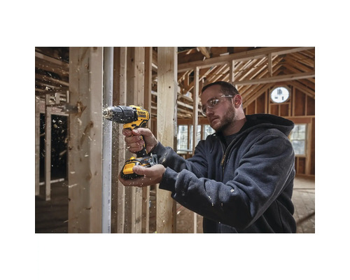 Řemeslník vrtá vrtačkou Dewalt do dřeva v hrubé stavbě.