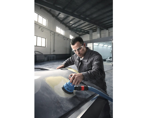 Muž brousí kapotu auta excentrickou bruskou v dílně.