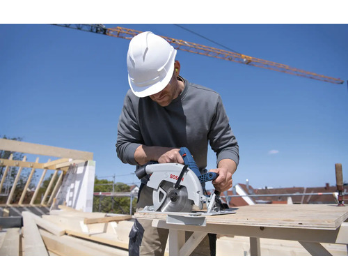 Řemeslník s ochrannou helmou řeže dřevo okružní pilou Bosch na staveništi.