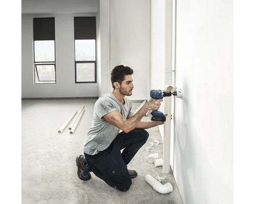 Řemeslník vrtá otvor akumulátorovým šroubovákem do zdi pro instalaci potrubí