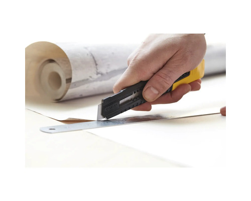 Ruka řeže tapetu nožem a pravítkem.