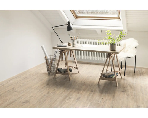 Světlá místnost se střešním oknem, světlou dřevěnou podlahou, psacím stolem na kozách a pracovními materiály