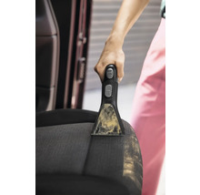 Detailní záběr osoby čistící autosedačku pomocí přenosného čističe skvrn.