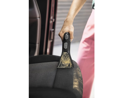 Detailní záběr osoby čistící autosedačku pomocí přenosného čističe skvrn.