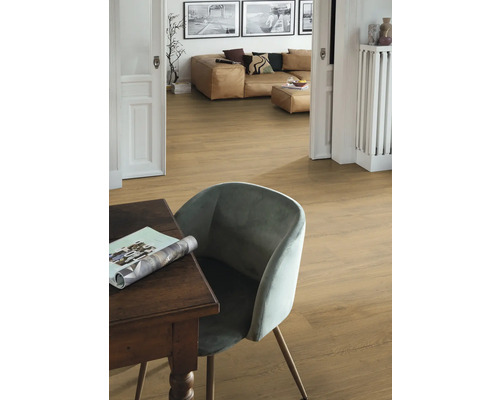 Interiérová fotografie místnosti s dřevěnou podlahou, stolem, židlí a obývacím prostorem v pozadí.