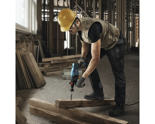 Stavební dělník vrtá s příklepovou vrtačkou do dřevěné desky.