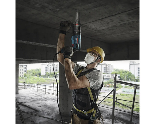 Stavební dělník vrtá s vrtacím kladivem do betonového stropu na staveništi.